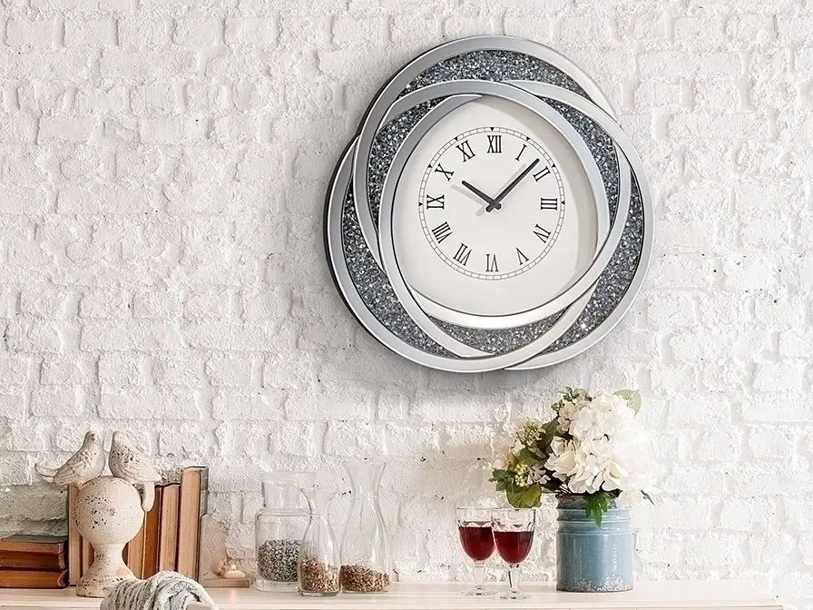 A sleek metal clock in a modern kitchen with stainless steel appliances.